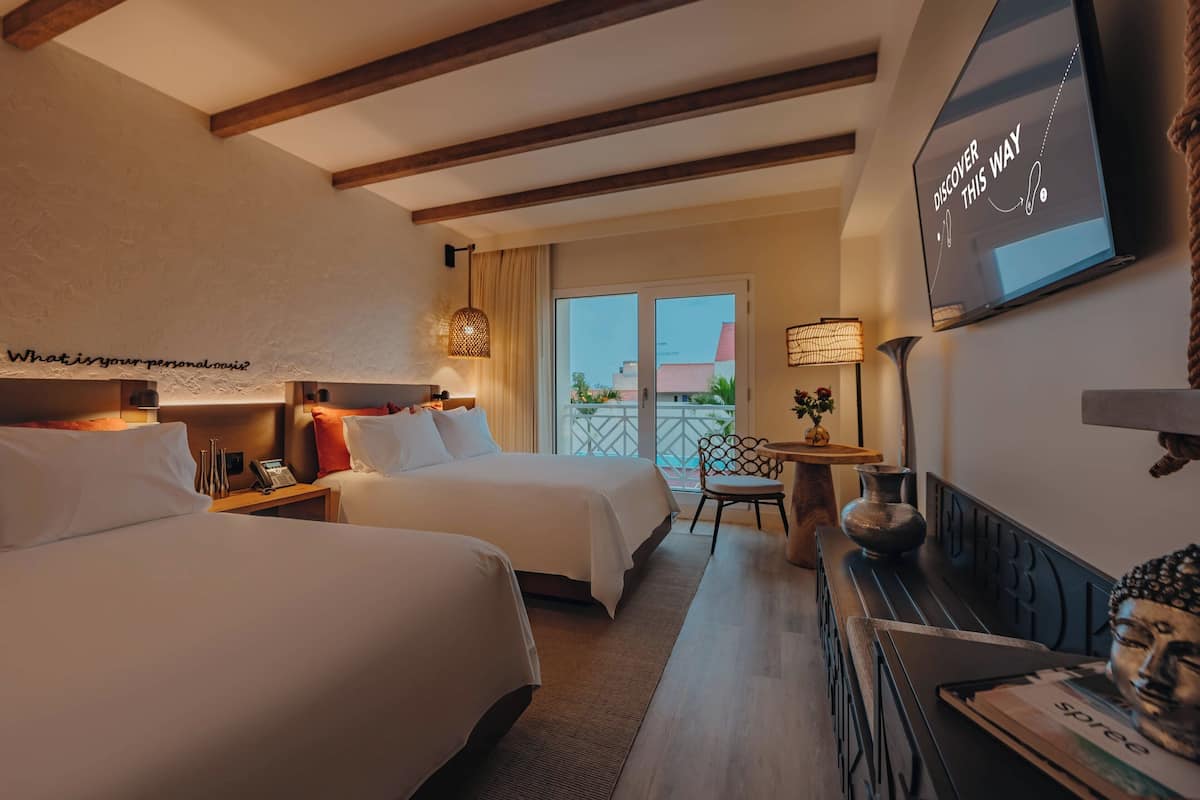 A hotel room with two beds, a television, a desk, and a balcony with a view.