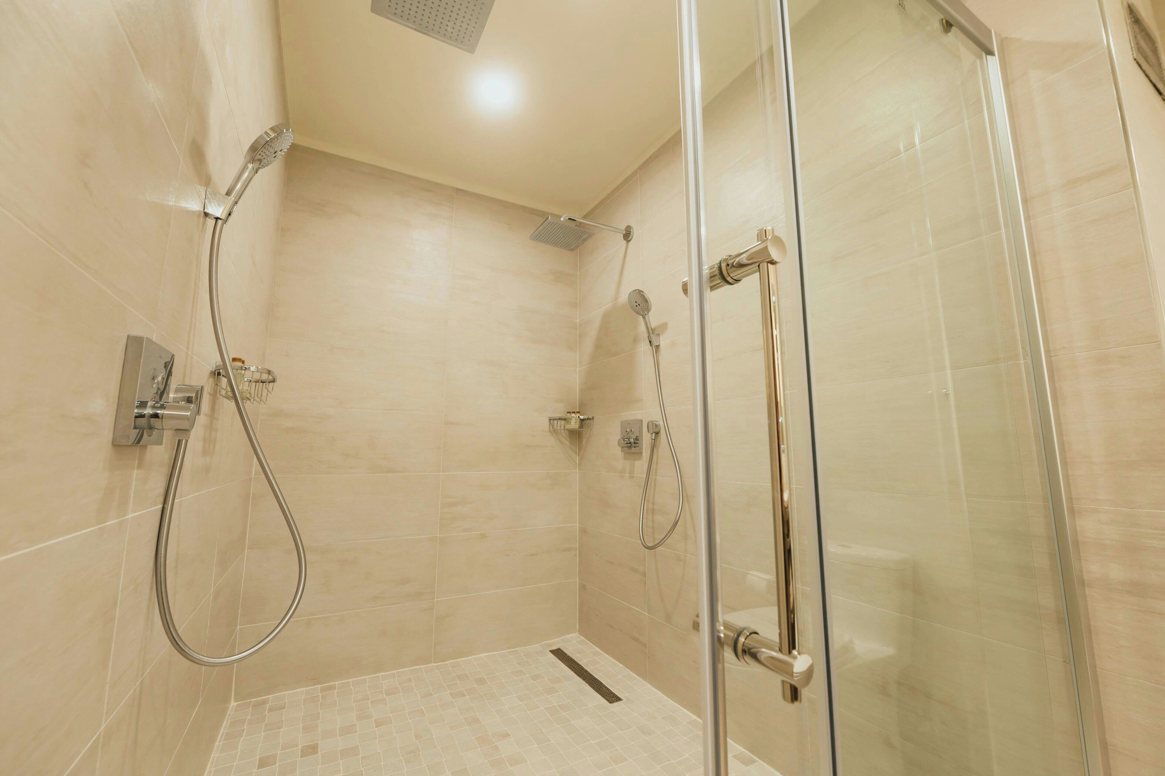 A modern shower area with a glass door, a handheld showerhead, and a wall-mounted control panel.