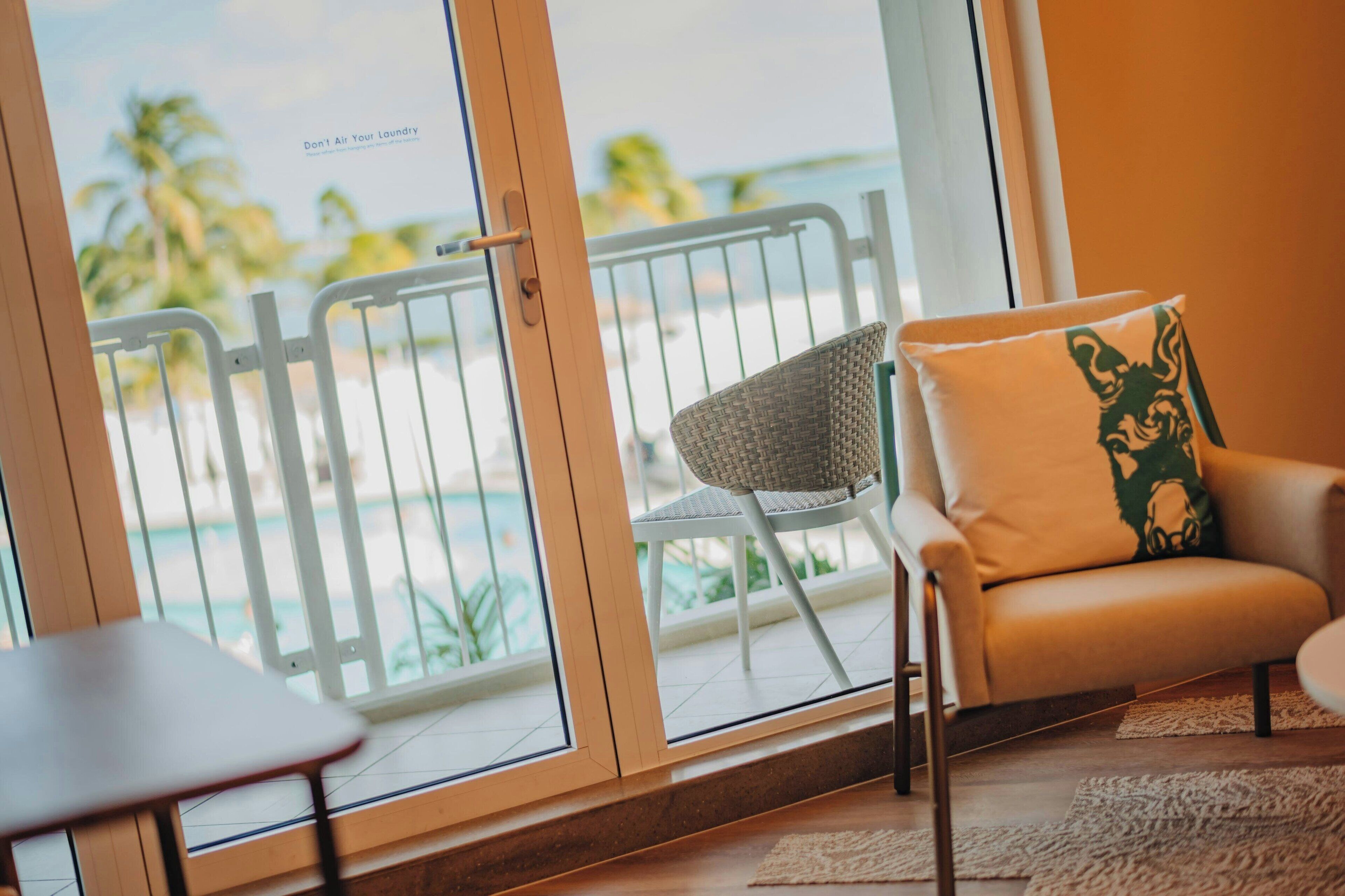 Una habitación con vistas a la playa, una silla con cojín y una mesita.