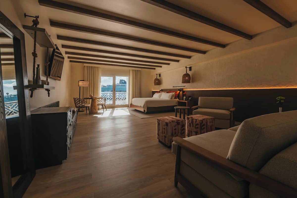 A hotel room with a bed, a sofa, a desk, and a balcony with a view.