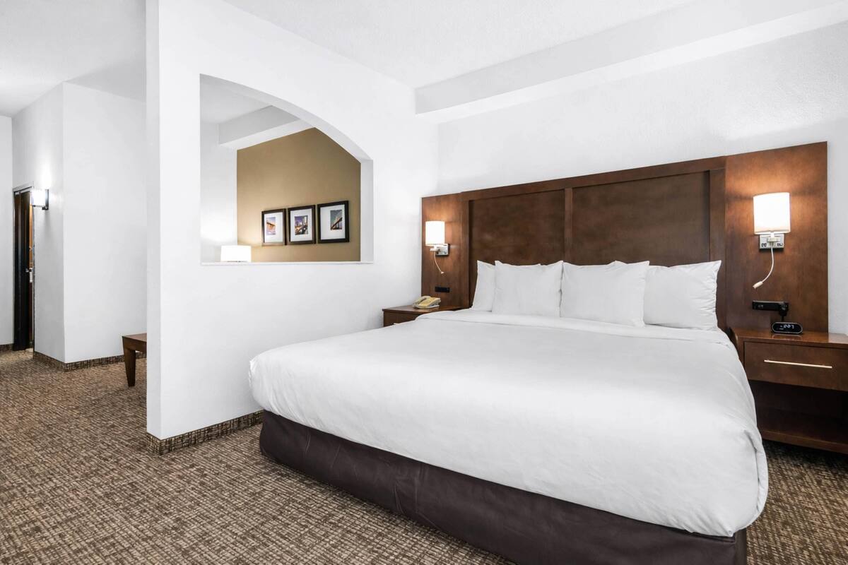 Hotellihuone, jossa on suuri sänky, yöpöytä, seinään kiinnitetty lamppu ja sängyn yläpuolella oleva kehystetty kuva.