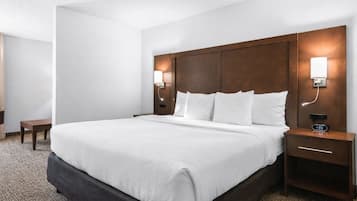 Une chambre d’hôtel avec un grand lit, deux tables de chevet, une petite table avec une horloge et des lampes fixées au mur.