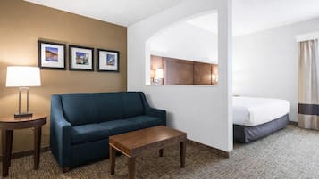 Habitación de hotel con sofá azul, mesa de centro de madera, cama, lámpara y cuadros en la pared.