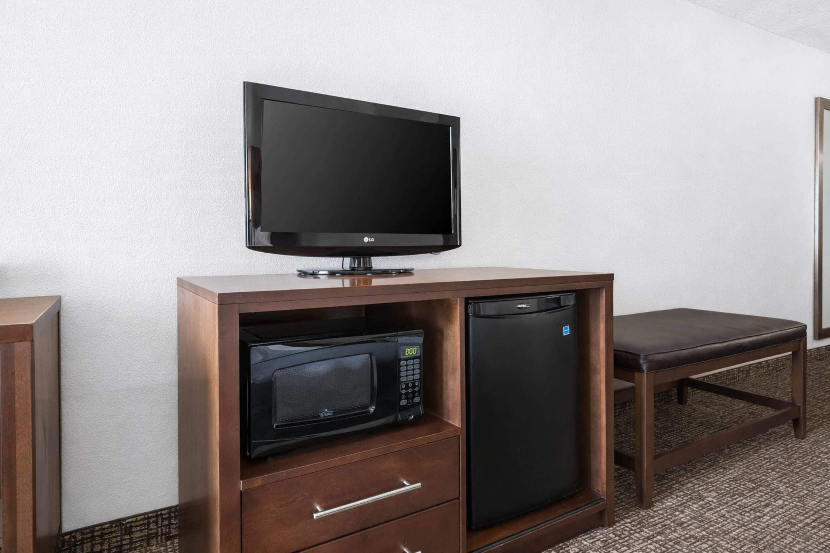 A hotel room with a flat-screen TV, a microwave, and a refrigerator.
