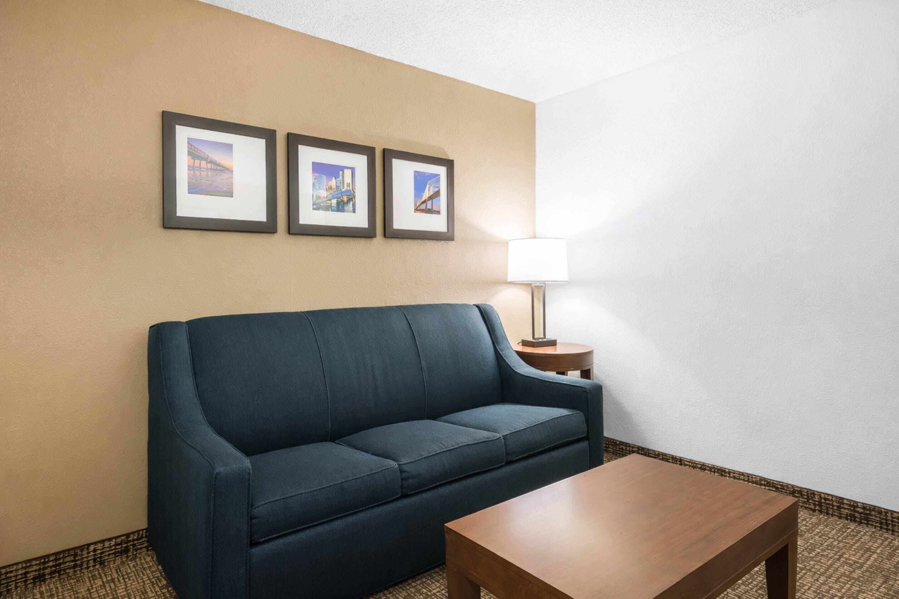 A room with a dark blue sofa, a wooden coffee table, a lamp on a side table, and three framed pictures on the wall.