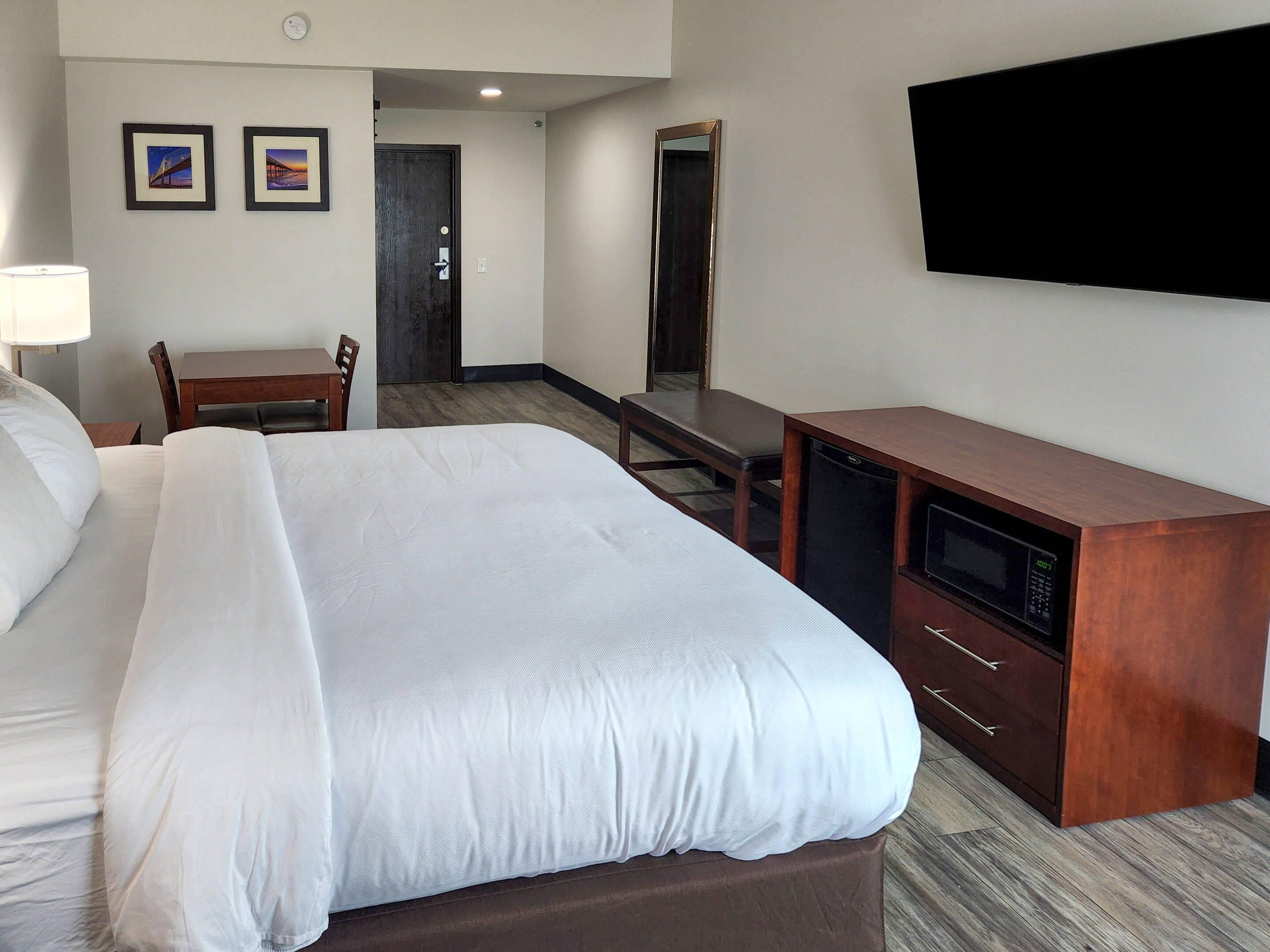 A hotel room with a bed, a desk, a chair, a TV, and a microwave.