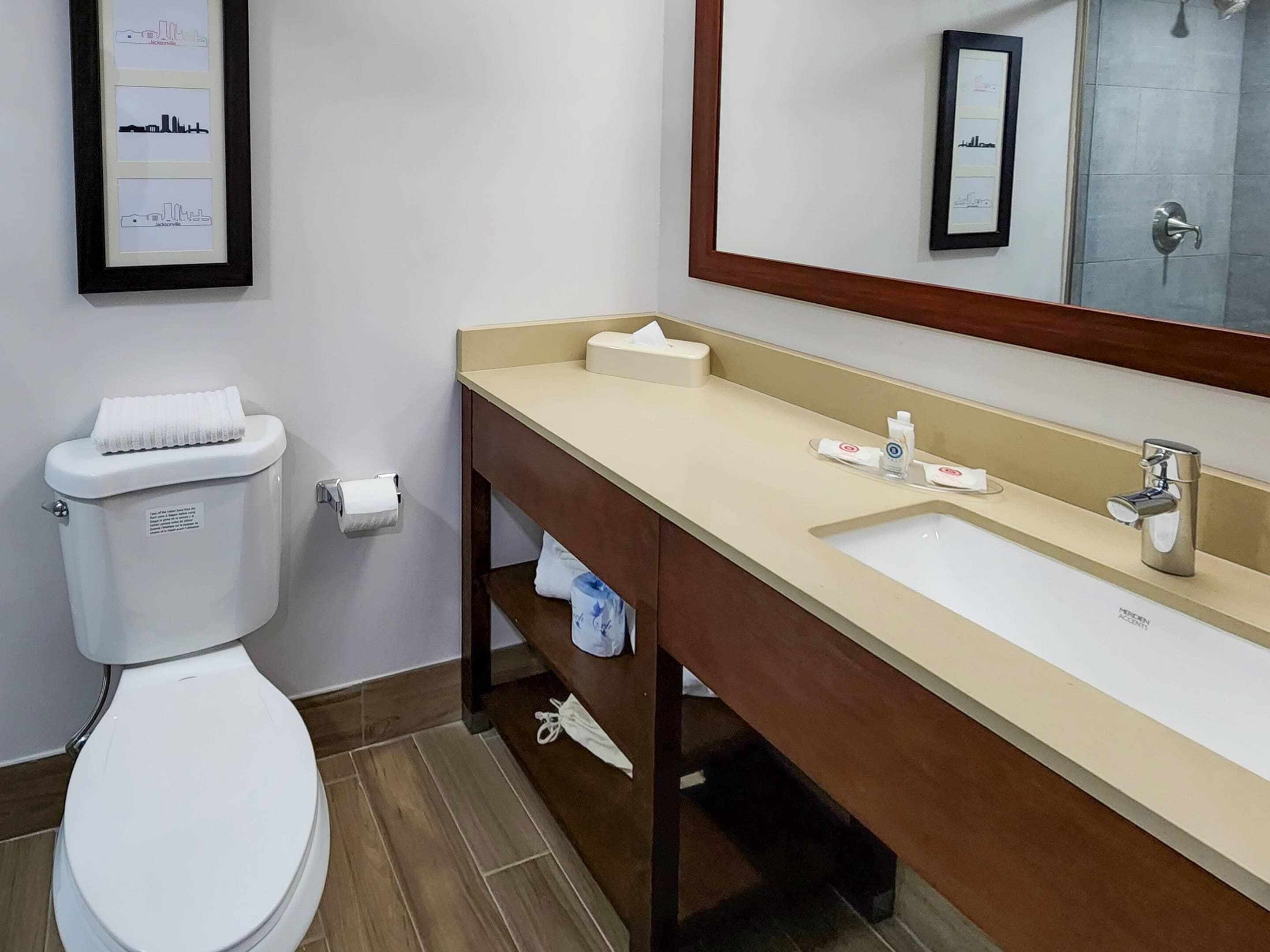 A bathroom with a toilet, sink, mirror, and framed cityscape pictures on the wall.