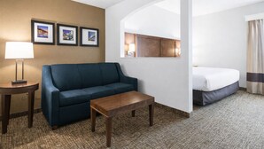 A hotel room with a sofa, a small table, a lamp, a bed, and framed pictures on the wall. - Comfort Suites Baymeadows Near Butler Blvd (Jacksonville)