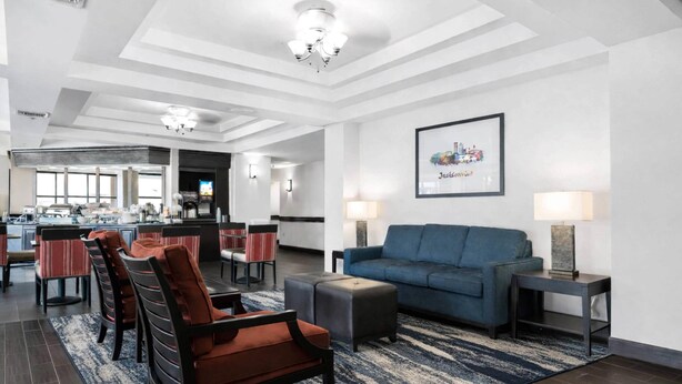 A modern hotel lobby with a dining area, a blue sofa, and a framed cityscape picture on the wall. - Comfort Suites Baymeadows Near Butler Blvd (Jacksonville)