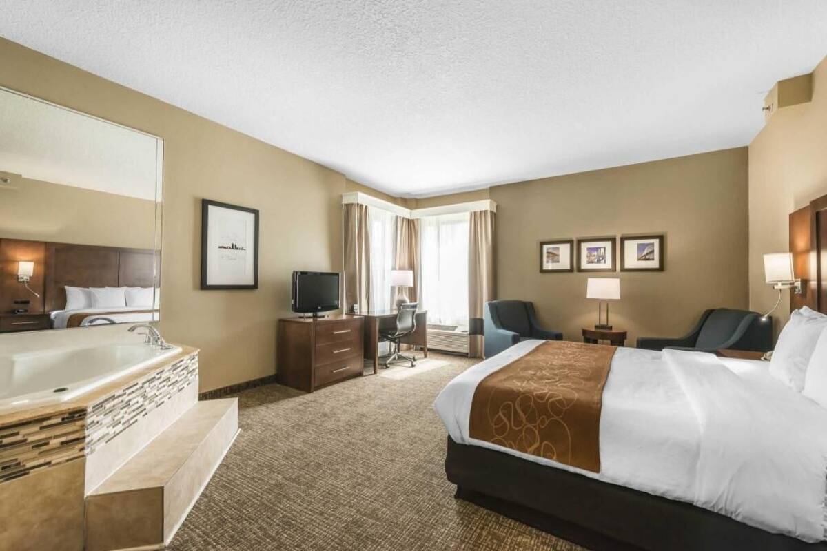 Una habitación de hotel con una cama grande, un baño con bañera, un escritorio con silla, televisión y cuadros en la pared.