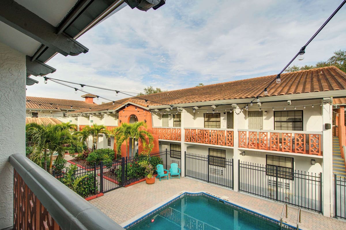 Un patio con piscina, mobiliario exterior y un edificio de varios pisos con balcones.