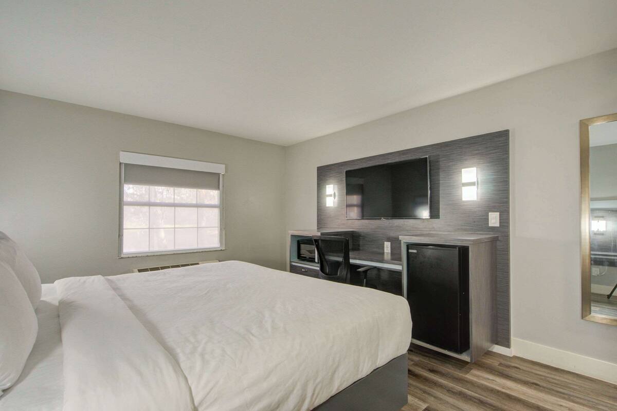 Un dormitorio con cama, escritorio, silla, televisión y ventana.