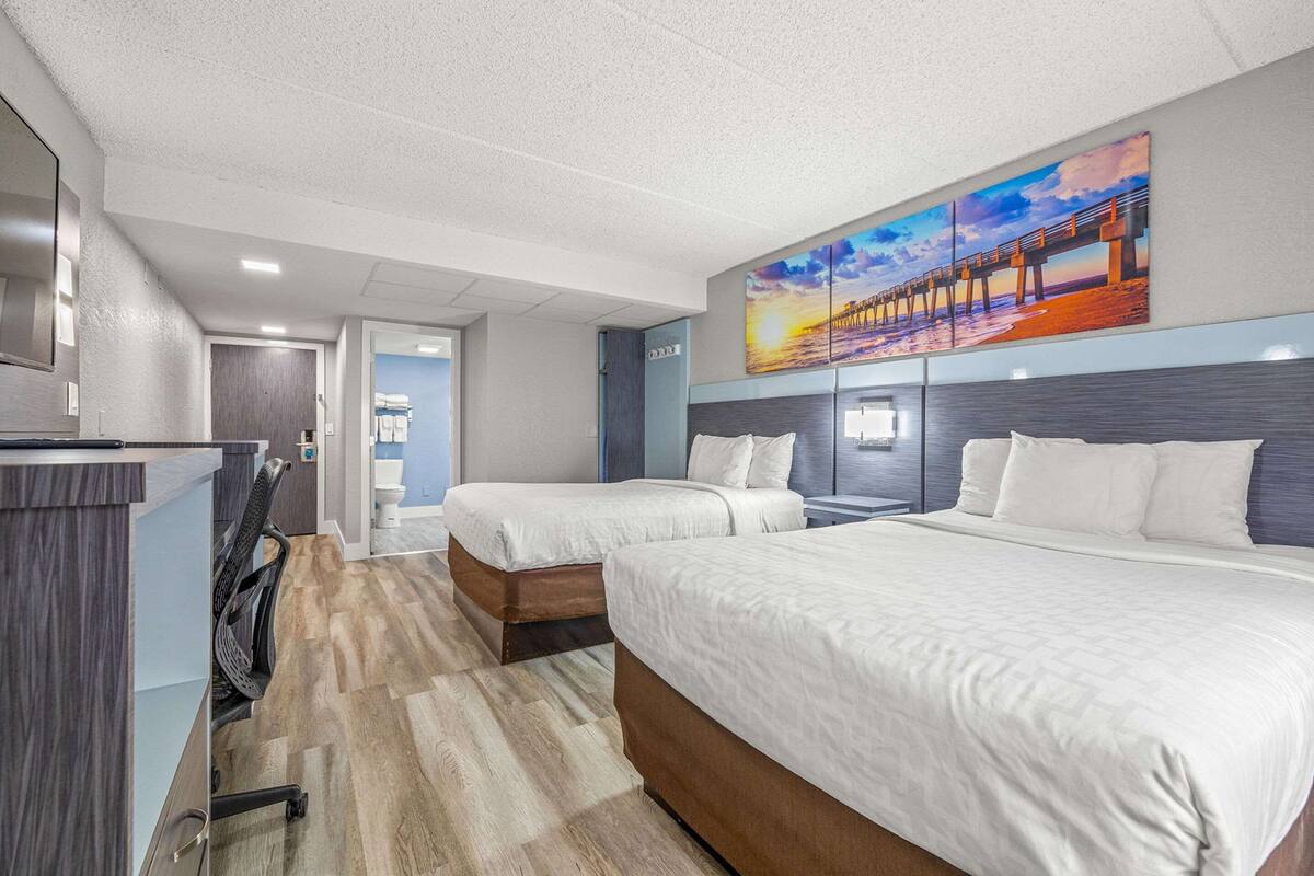 Habitación de hotel con dos camas, un escritorio y un cuadro grande de un muelle en la pared.