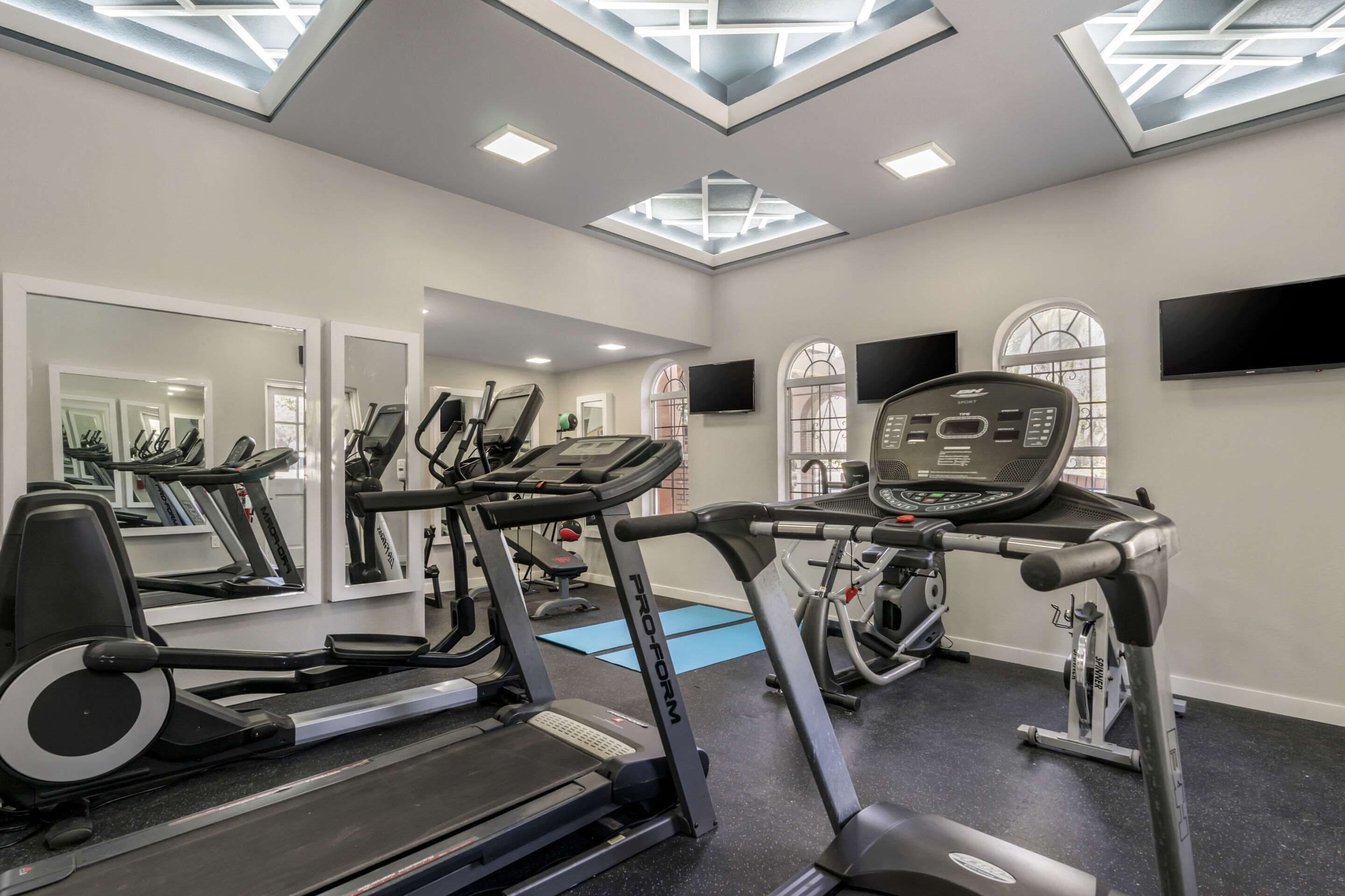 A gym with treadmills, exercise bikes, and a mirrored wall.