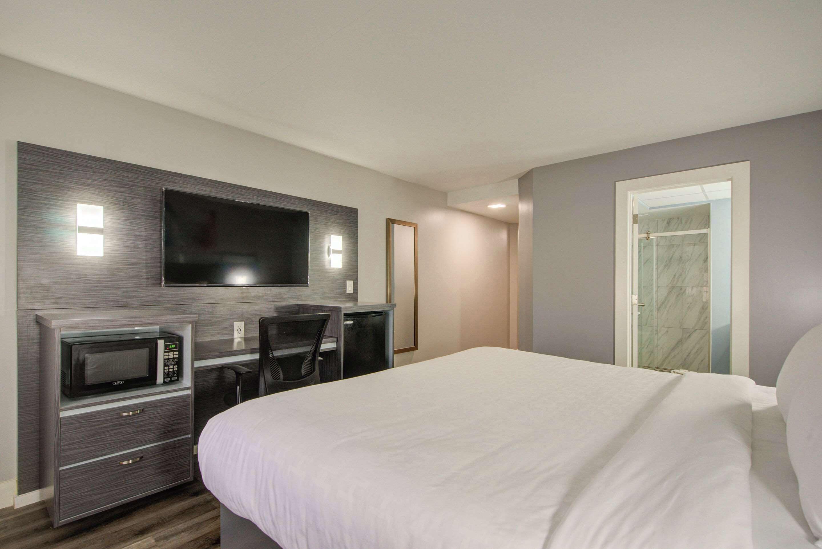 A hotel room with a bed, a TV mounted on the wall, a microwave, and a desk with a chair.