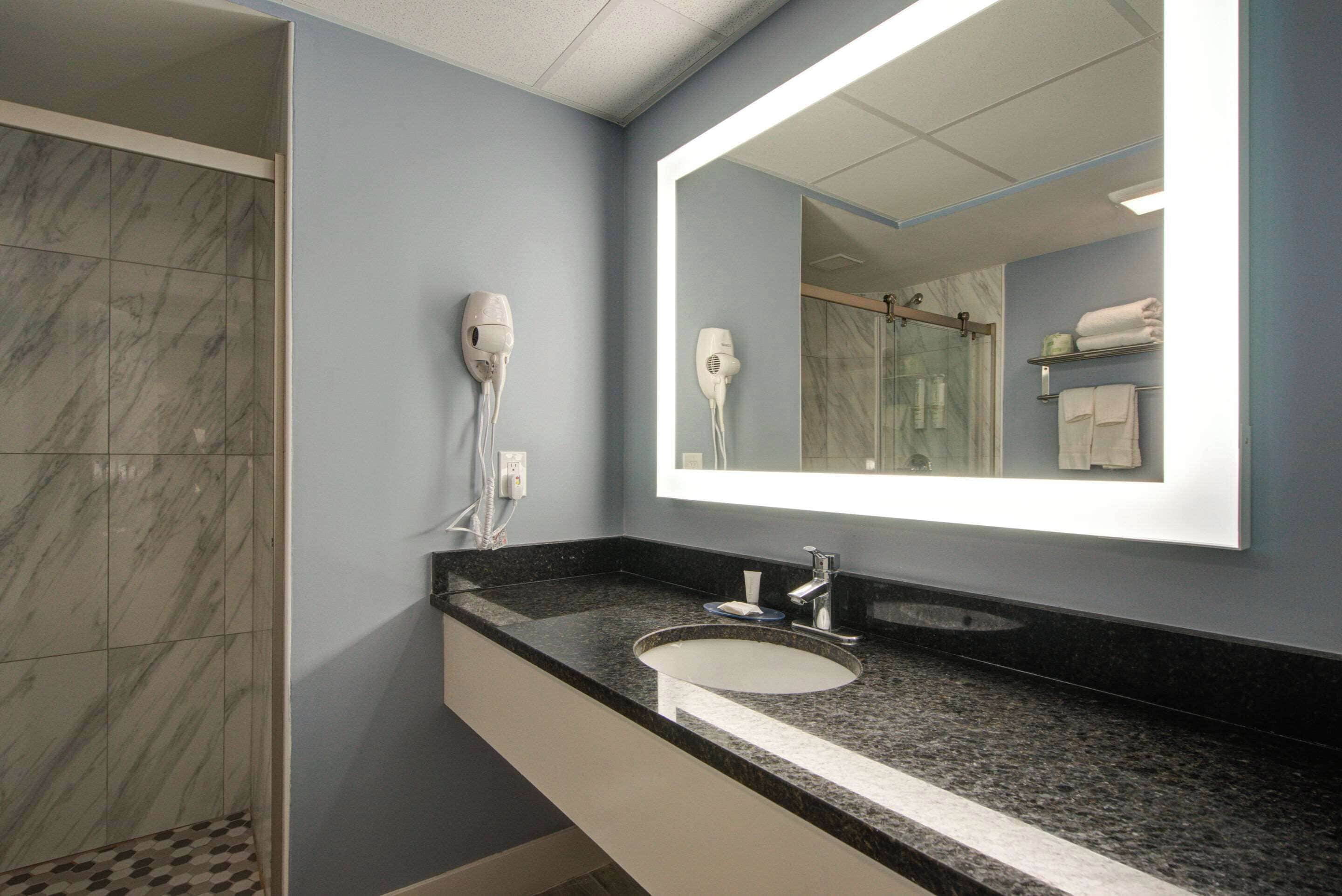 Un baño con ducha de mármol, lavabo con espejo y secador de pelo en la pared.
