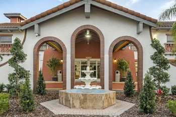 A hotel room with a large bed, a painting of a beach scene, a modern headboard, and a bathroom visible through an open door. at Clarion Pointe Tampa-Brandon Near Fairgrounds and Casino