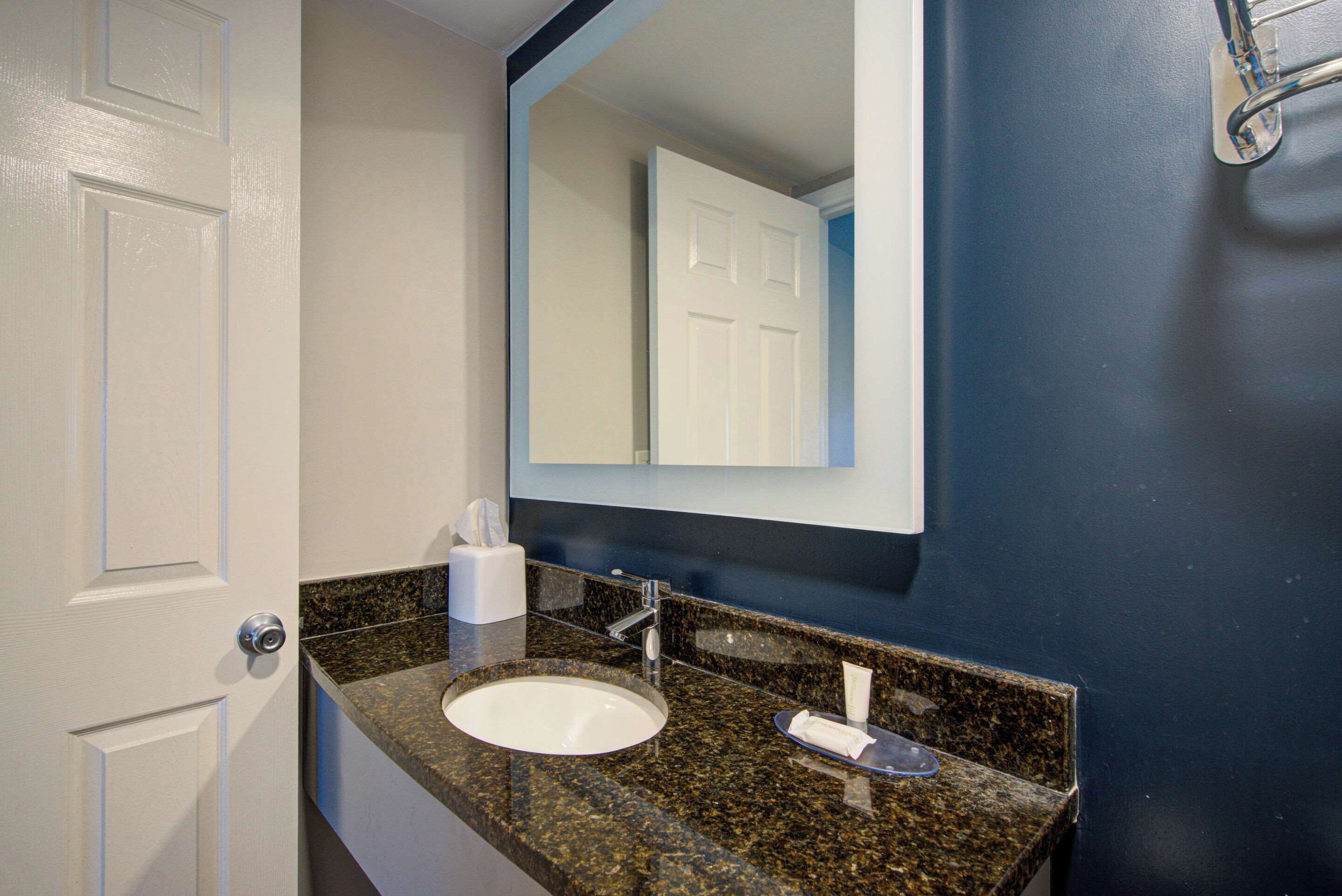 A bathroom with a white sink, a mirror, and a towel dispenser.