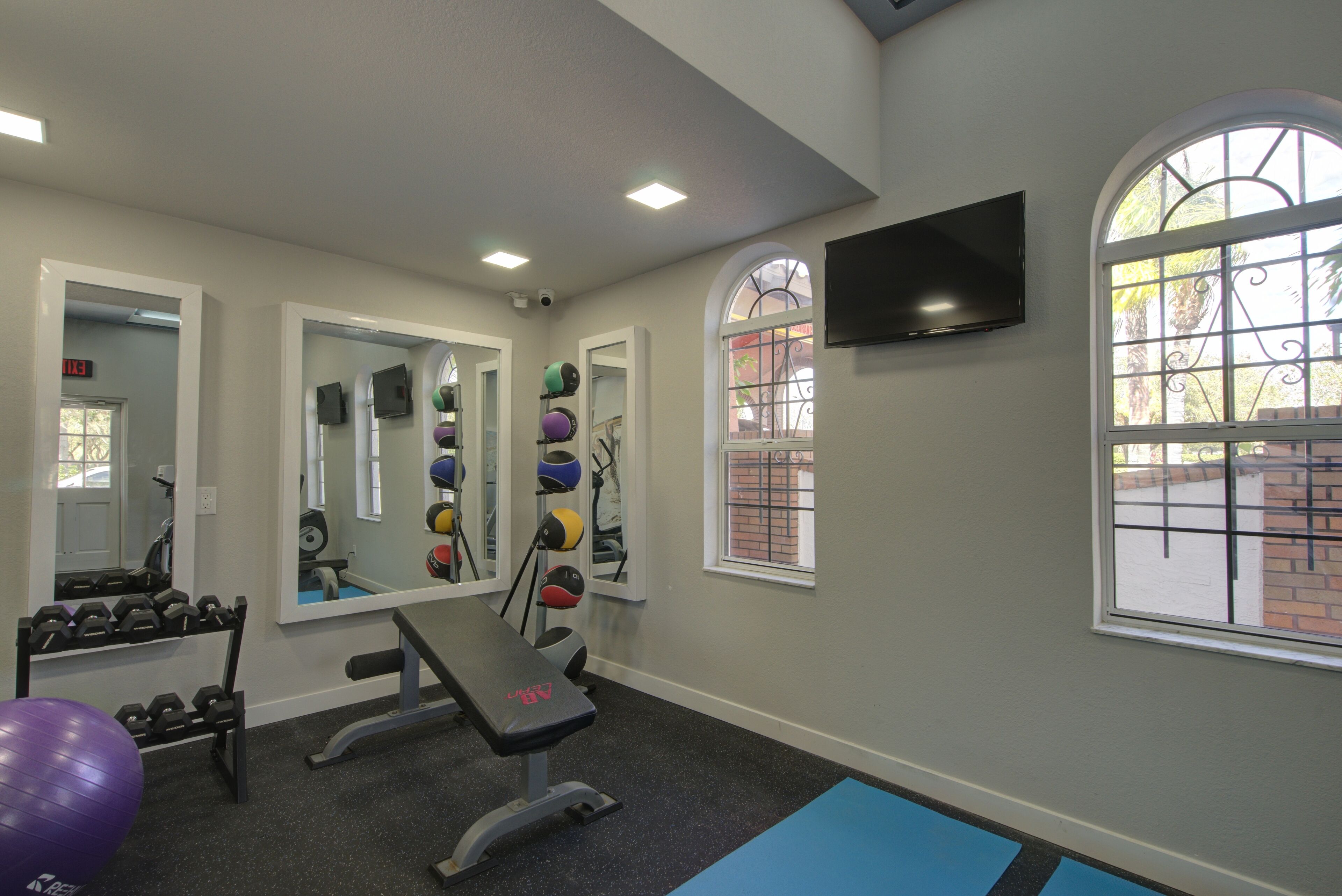 Une salle de sport équipée de matériel d’exercice, d’un banc, d’haltères et d’un grand miroir.