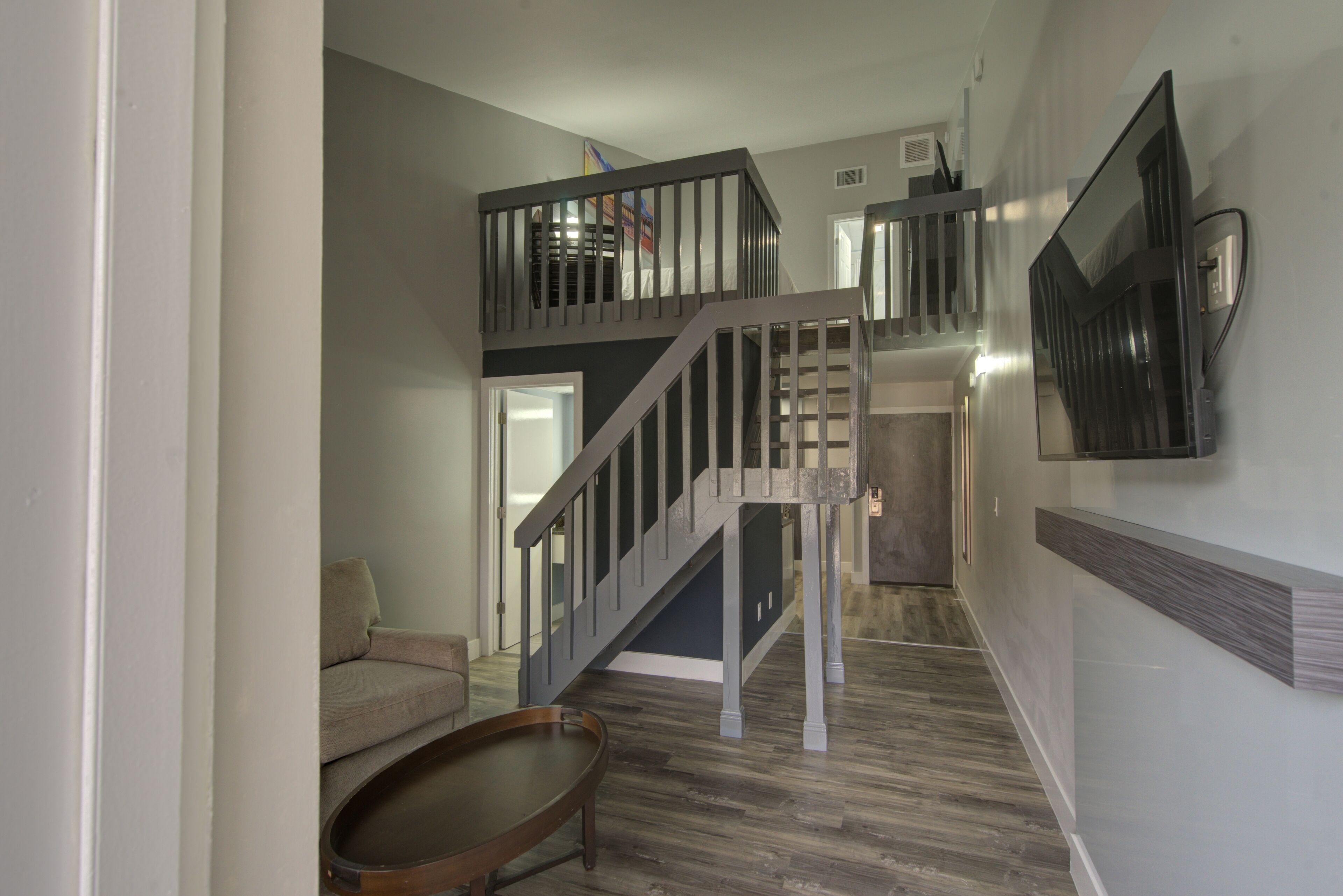 Ein modernes Interieur mit einer Treppe, die zu einer oberen Ebene führt, einem an der Wand montierten Flachbildfernseher und einem Holztisch im Vordergrund.