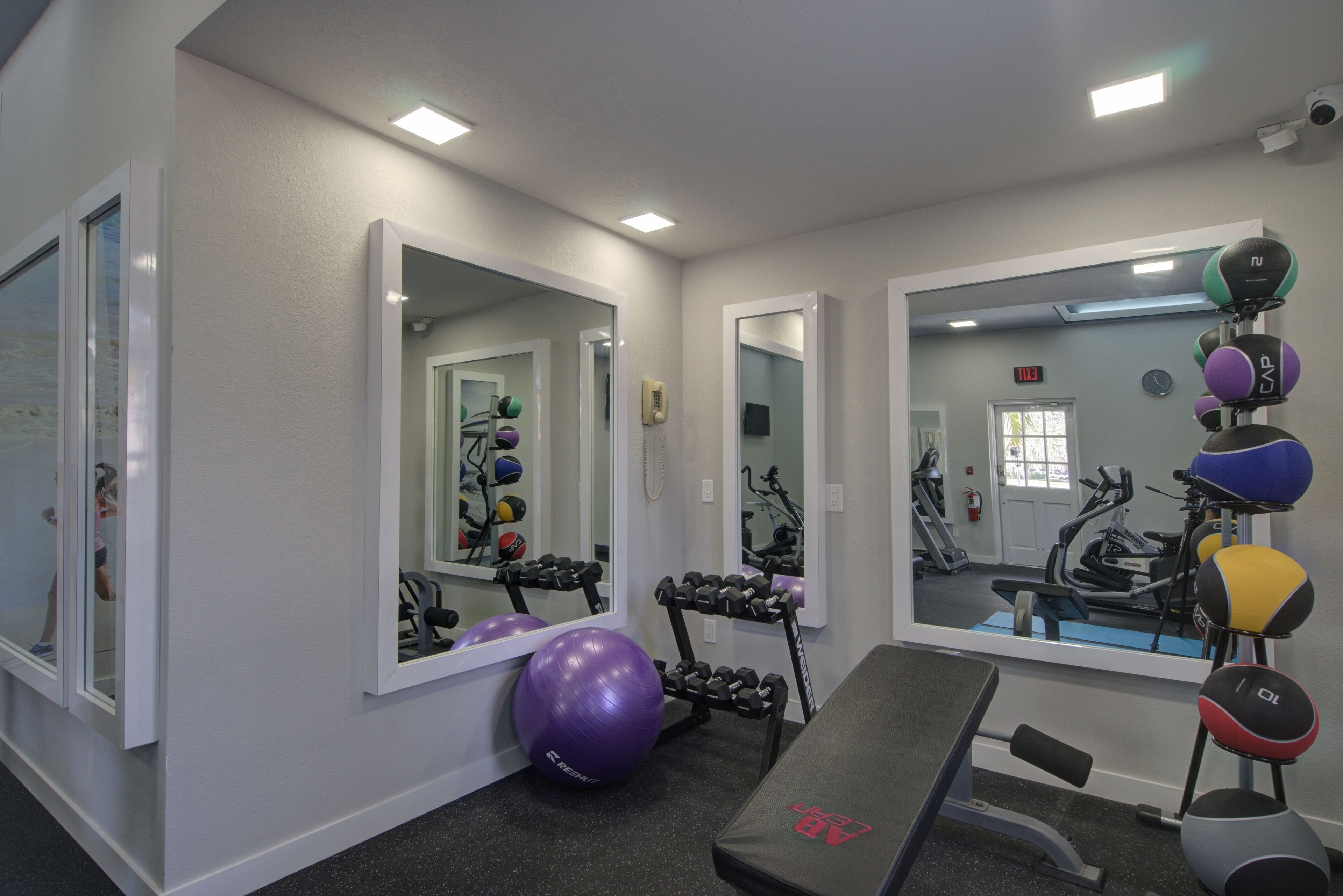A gym with exercise equipment, mirrors, and a bench.