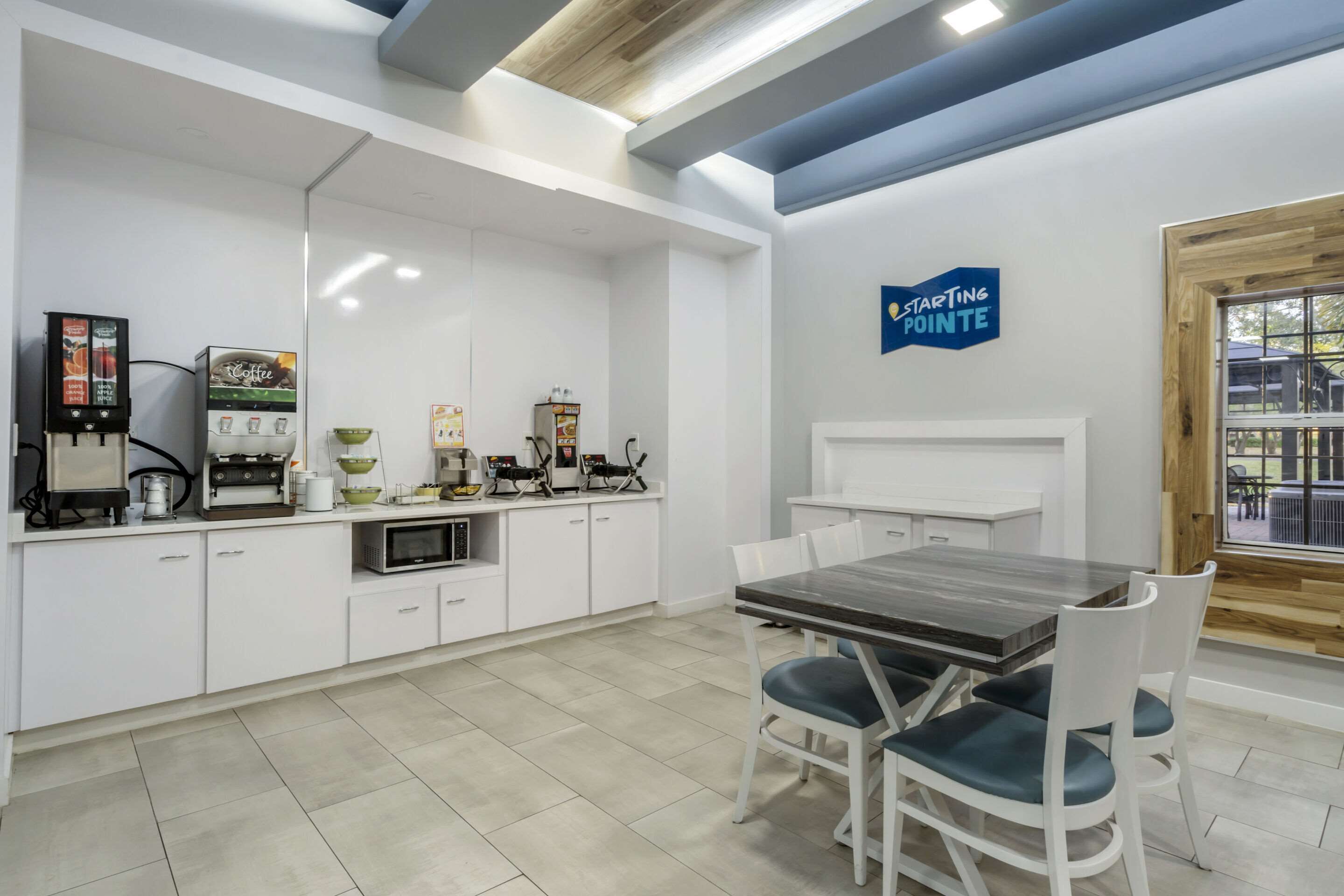A modern kitchen with white cabinetry, a coffee machine, a microwave, and a dining area with a wooden table and chairs.