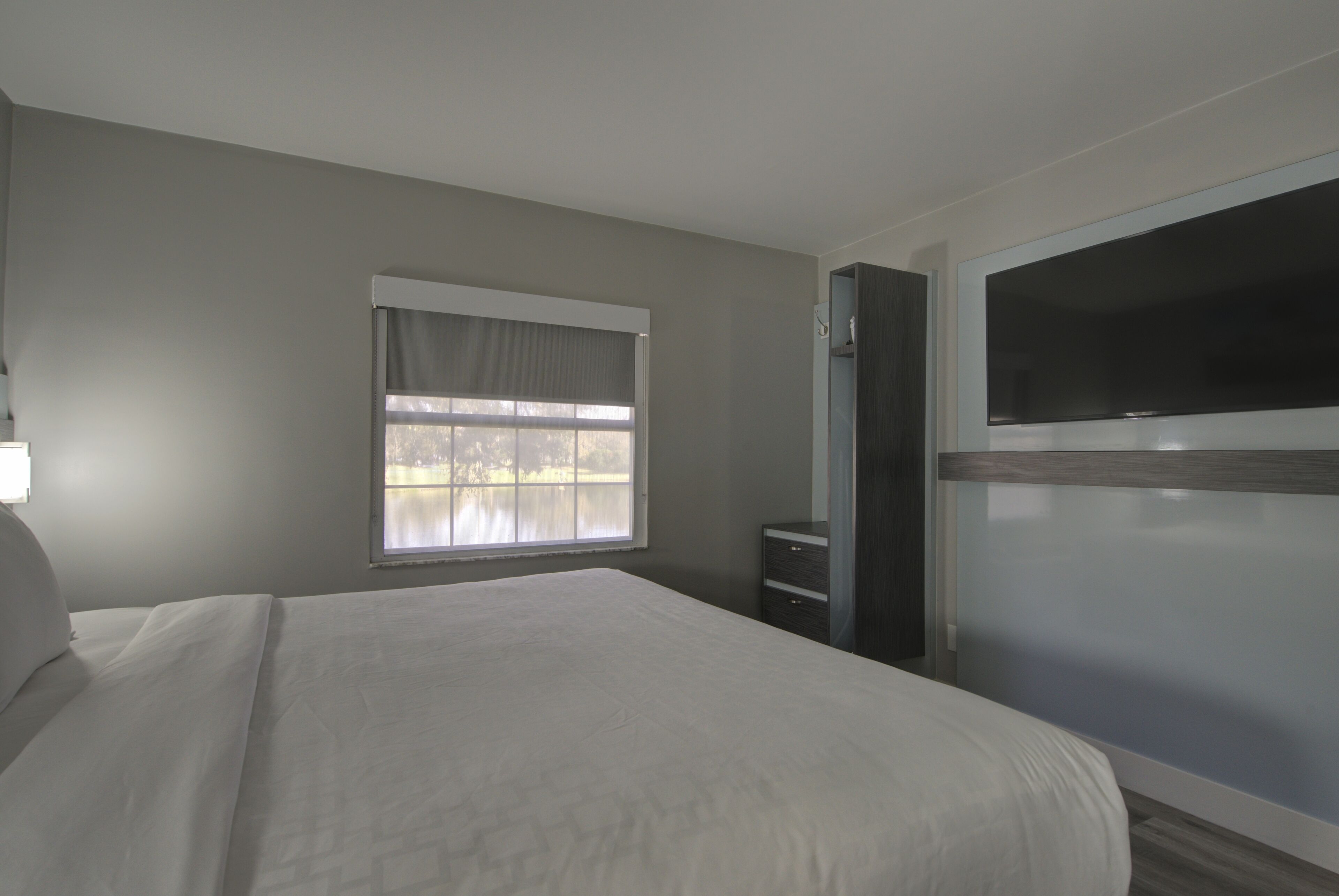 Een slaapkamer met een groot bed, een raam met uitzicht, een dressoir en een aan de muur bevestigde televisie.