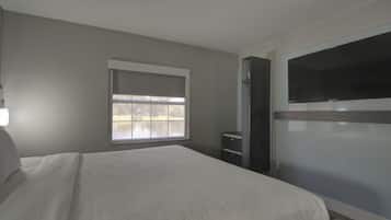 Een slaapkamer met een groot bed, een raam met uitzicht, een dressoir en een aan de muur bevestigde televisie.