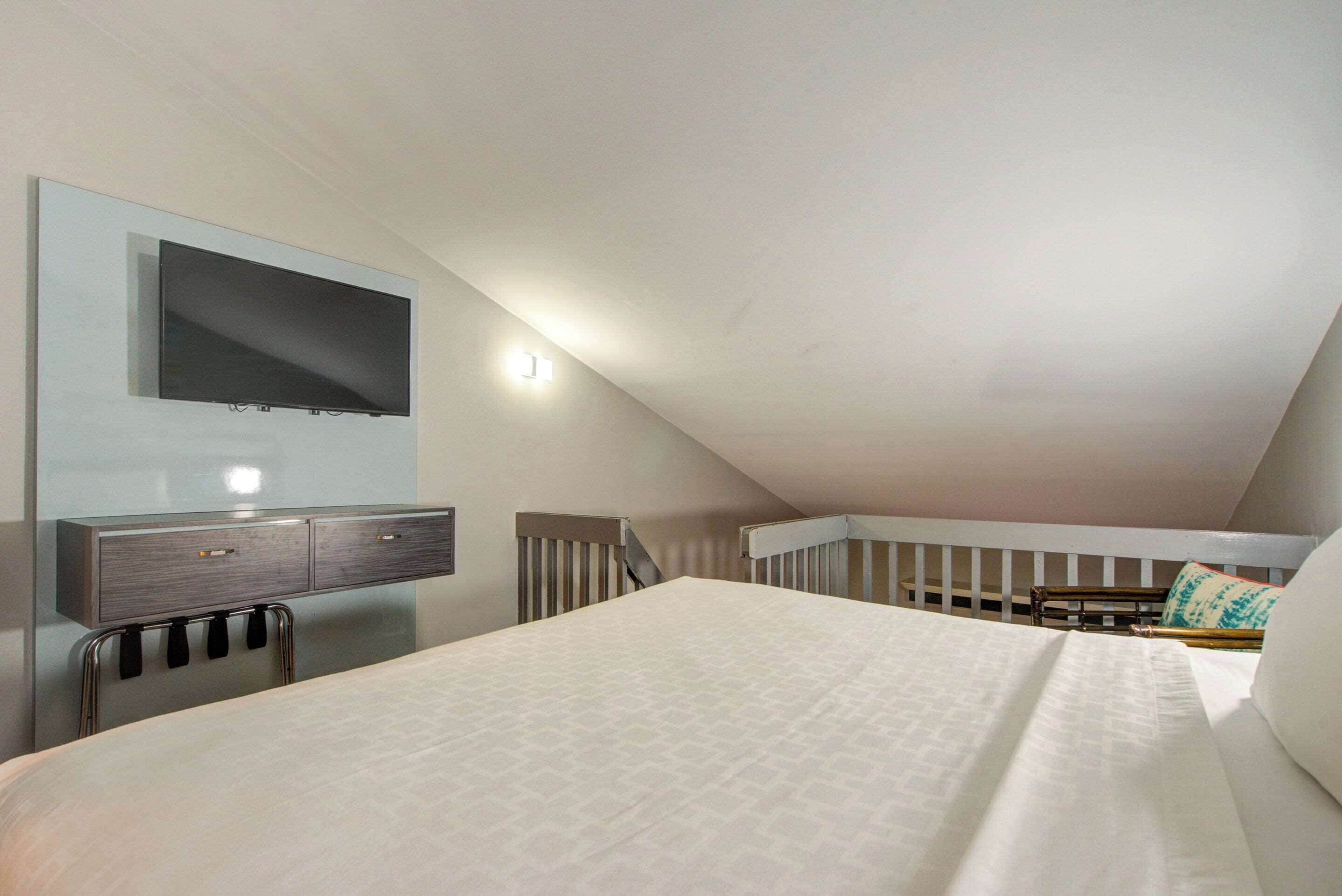 A modern bedroom with a large bed, a TV mounted on the wall, and a small desk with drawers.