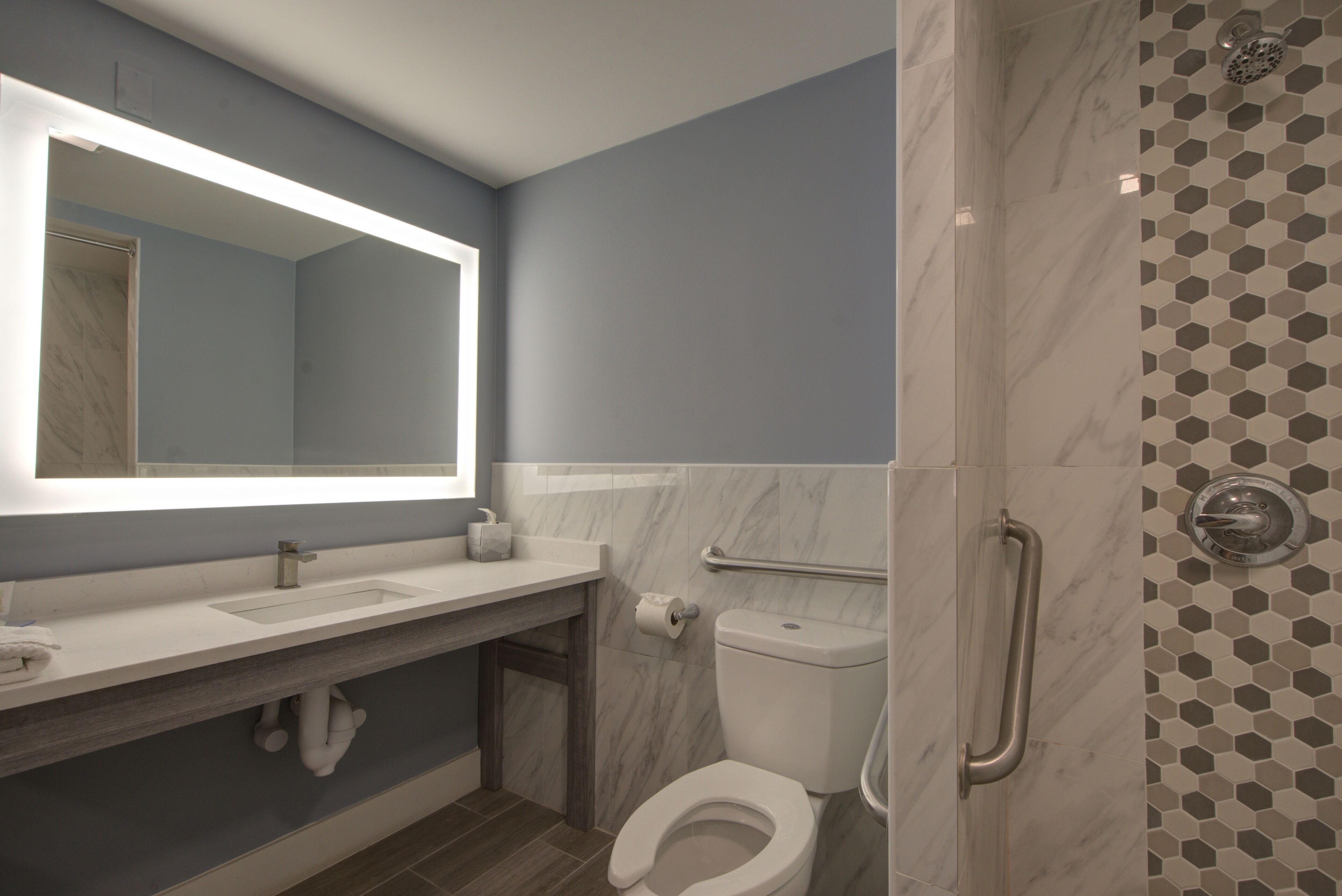 A modern bathroom with a marble sink, a toilet, and a shower with a hexagonal tile pattern.