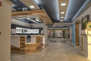 A modern dining area with marble tables and white chairs, a kitchen with white cabinets, and a ceiling with wooden panels and recessed lighting. at Clarion Pointe Tampa-Brandon Near Fairgrounds and Casino