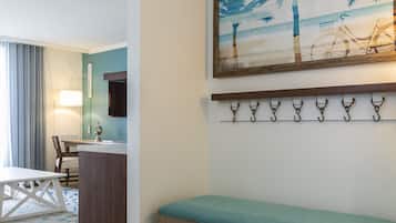 Habitación de hotel con un banco de madera, una mesa de comedor, una silla, una zona de cocina y un sistema de ganchos en la pared.