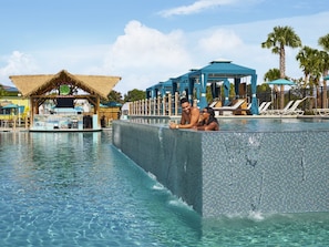 A couple relaxing in a clear, tiled infinity pool with a bar area and lounge chairs in the background. - Margaritaville Lake Resort, Lake Conroe/Houston (Montgomery)