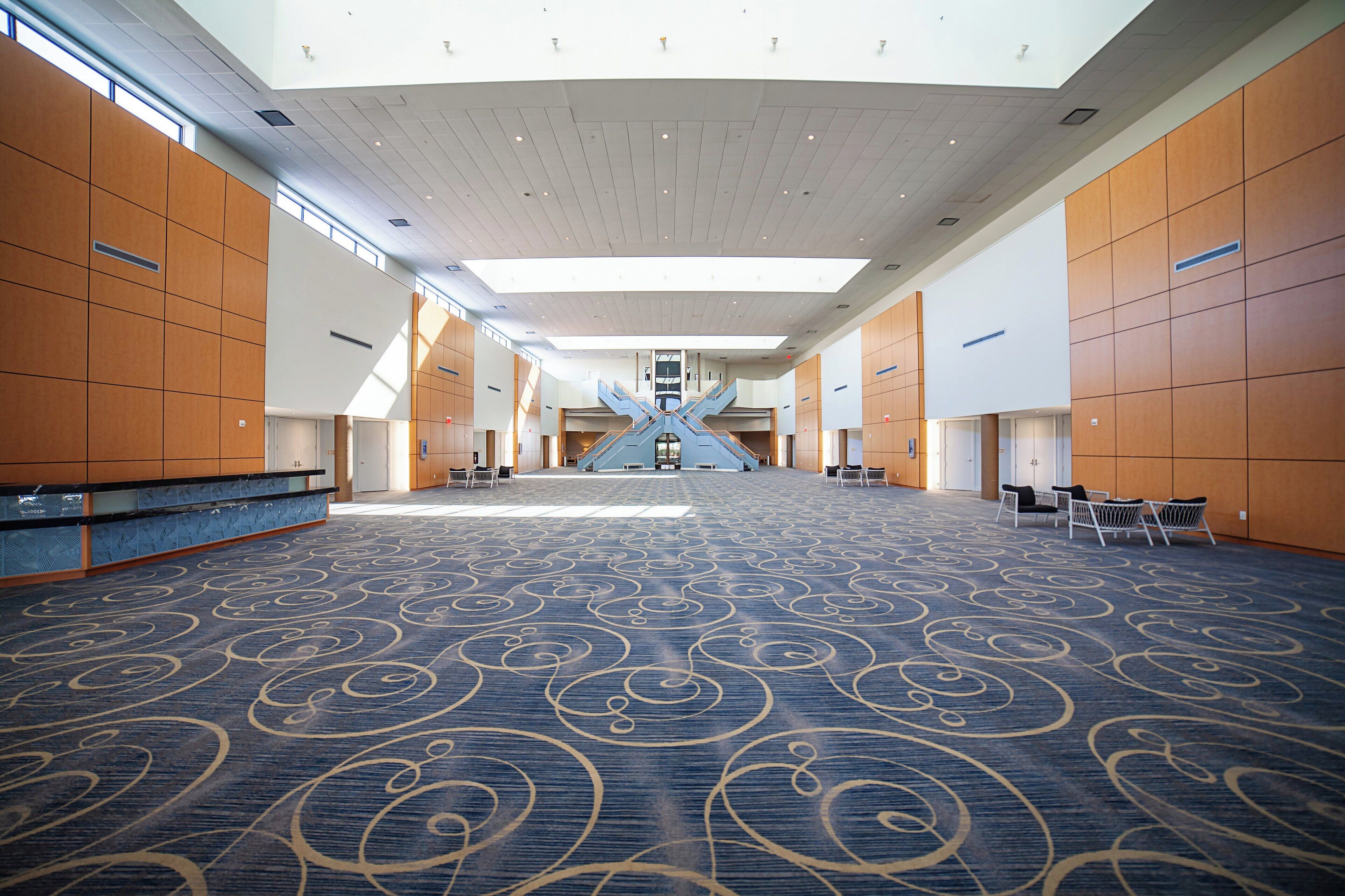 A spacious interior with a high ceiling, patterned carpet, and a central staircase.