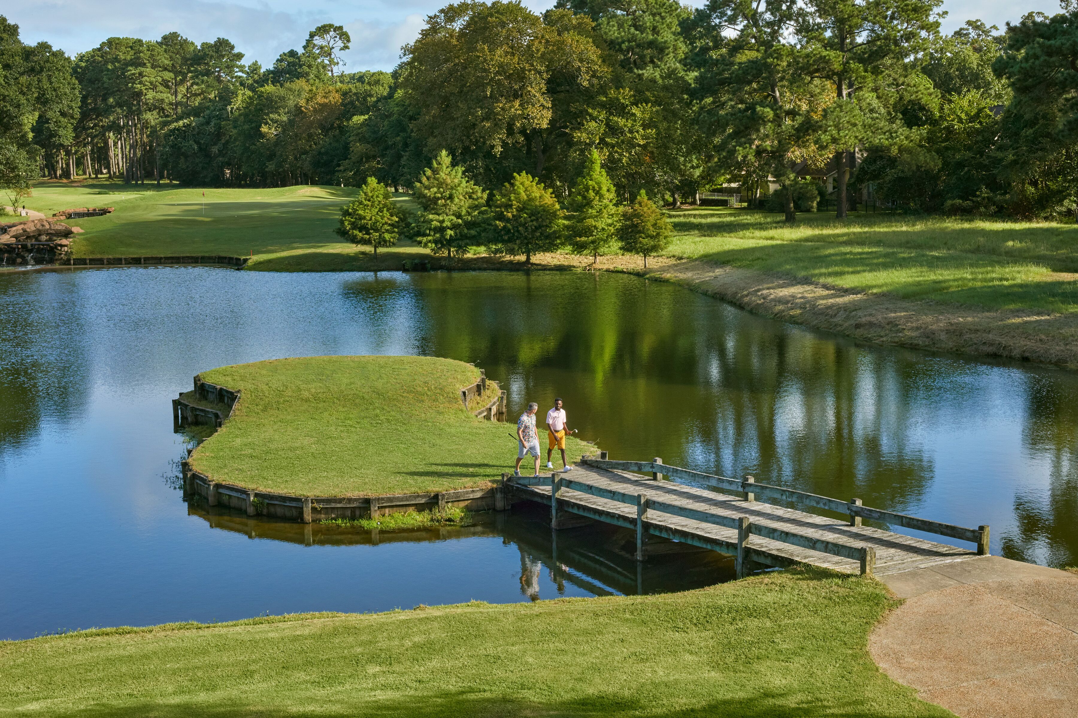 A golf course with a pond, a wooden bridge, and a well-maintained lawn.