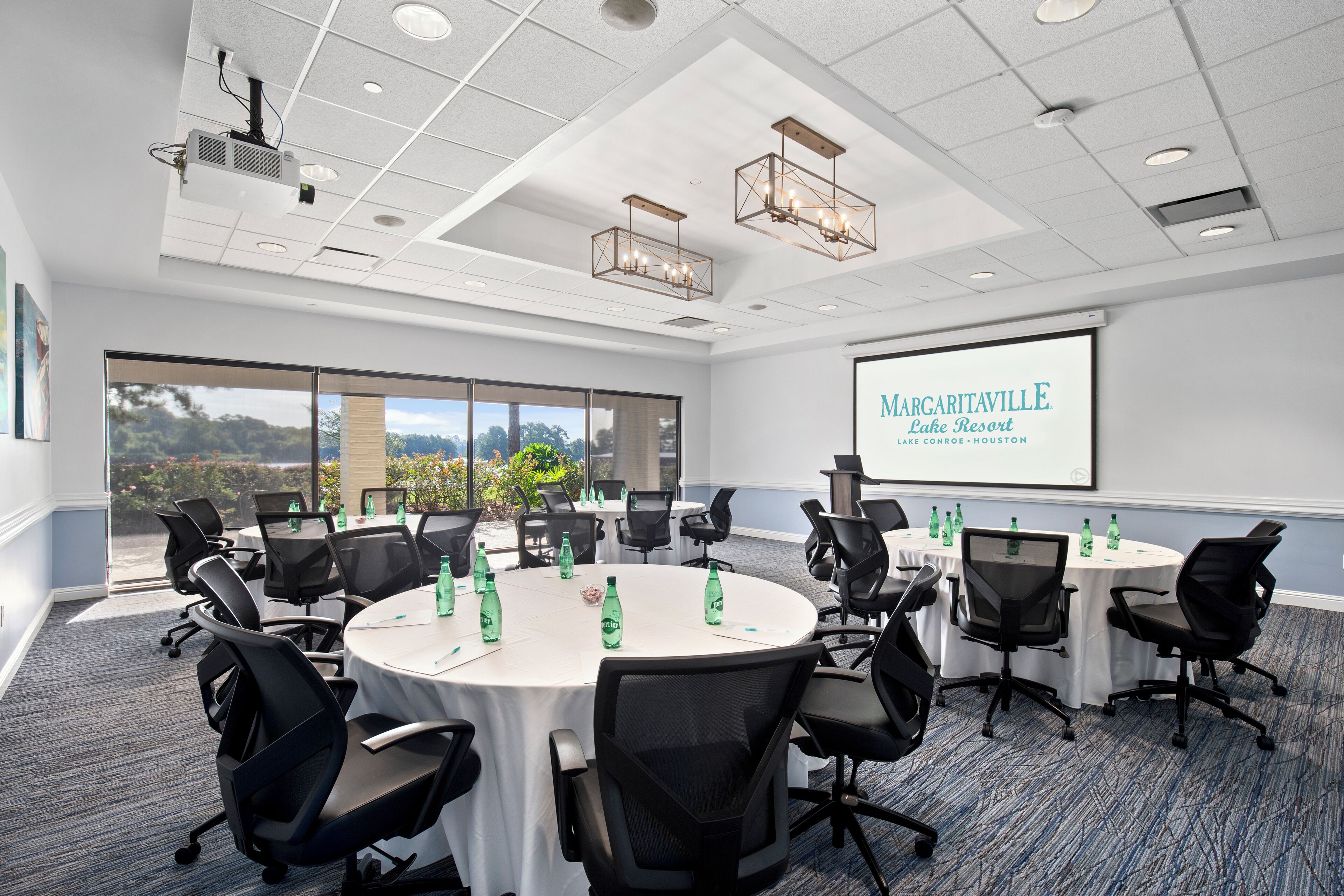 A conference room with round tables, black chairs, and a projector screen displaying 'Margaritaville Lake Resort'.