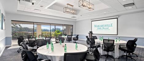A conference room with round tables, black chairs, and a projector screen displaying 'Margaritaville Lake Resort'.