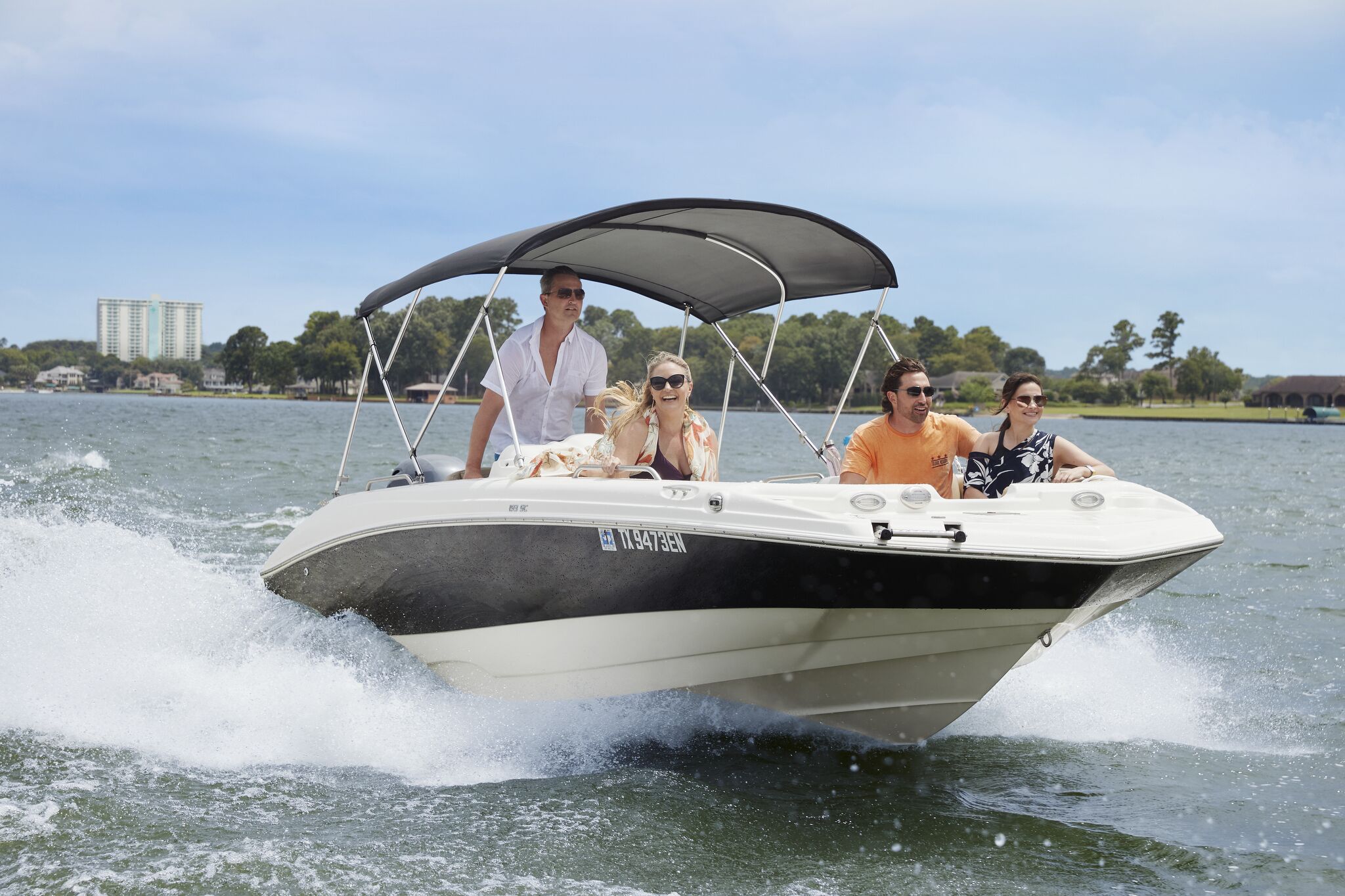 A boat with a canopy, passengers, and a water body with buildings in the background.