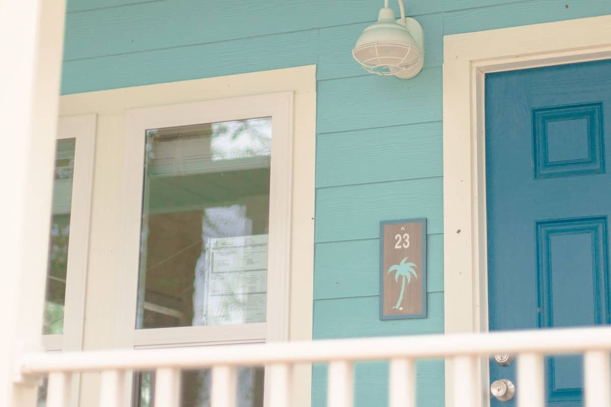 A blue door with a number plate, a white railing, and a light fixture on a teal wall.