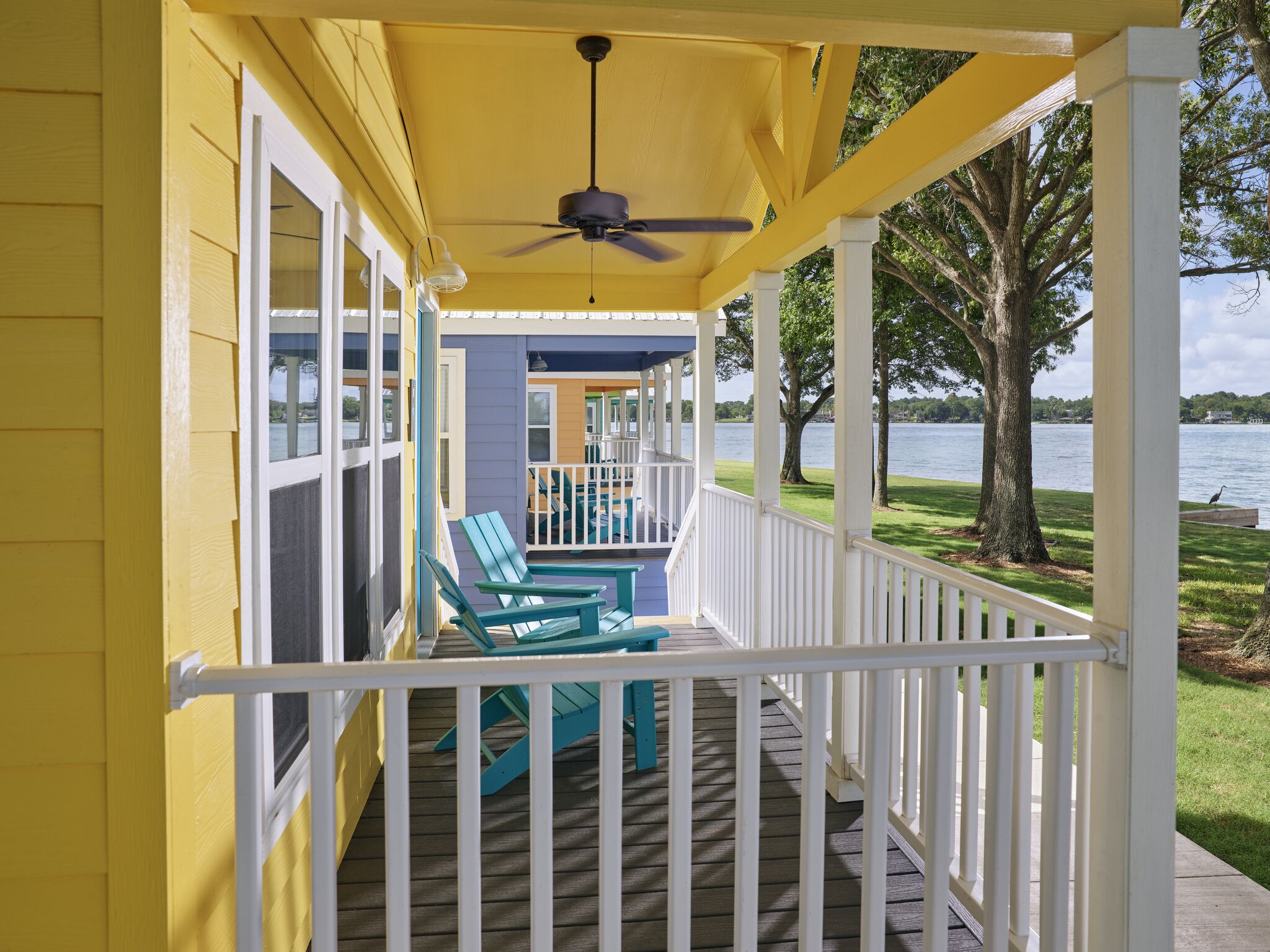 A covered porch with a ceiling fan, a view of a lake, and a grassy area with trees.