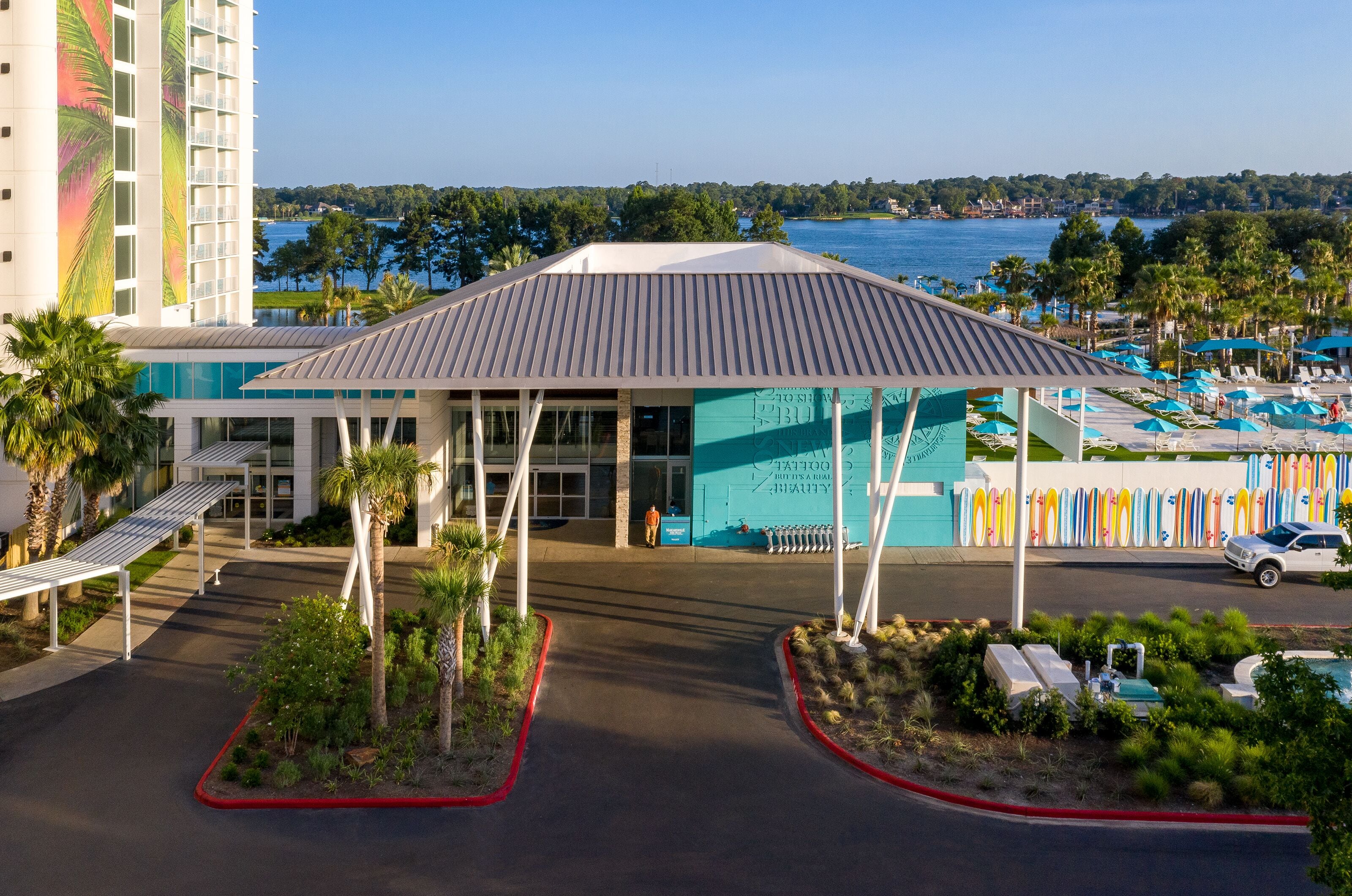 A hotel with a covered entrance, a pool area with lounge chairs, and a view of the water.
