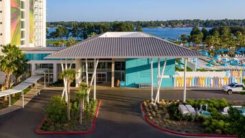 A hotel with a covered entrance, a pool area with lounge chairs, and a view of the water.