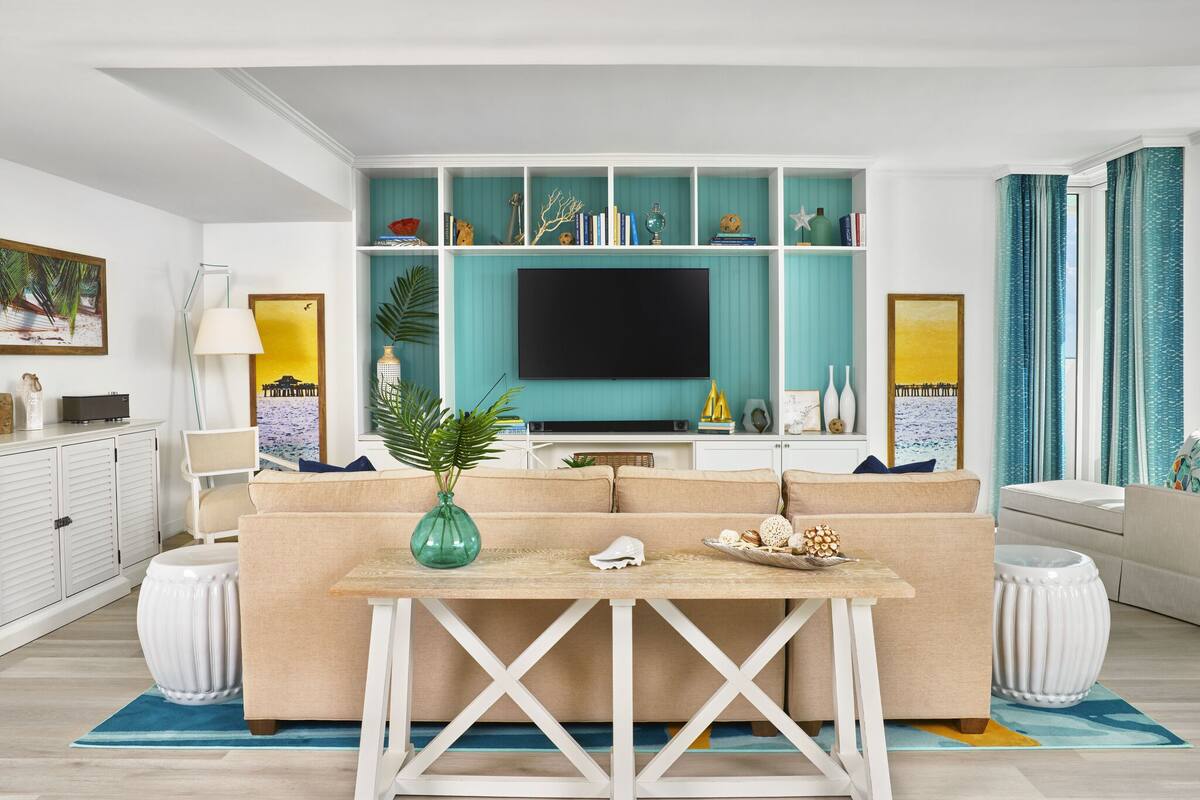 A modern living room with a beige sofa, a coffee table, and a TV against a teal wall.