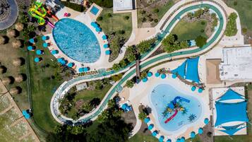 Vista aérea de un parque acuático con múltiples piscinas, senderos sinuosos y zonas de sombra con sombrillas.