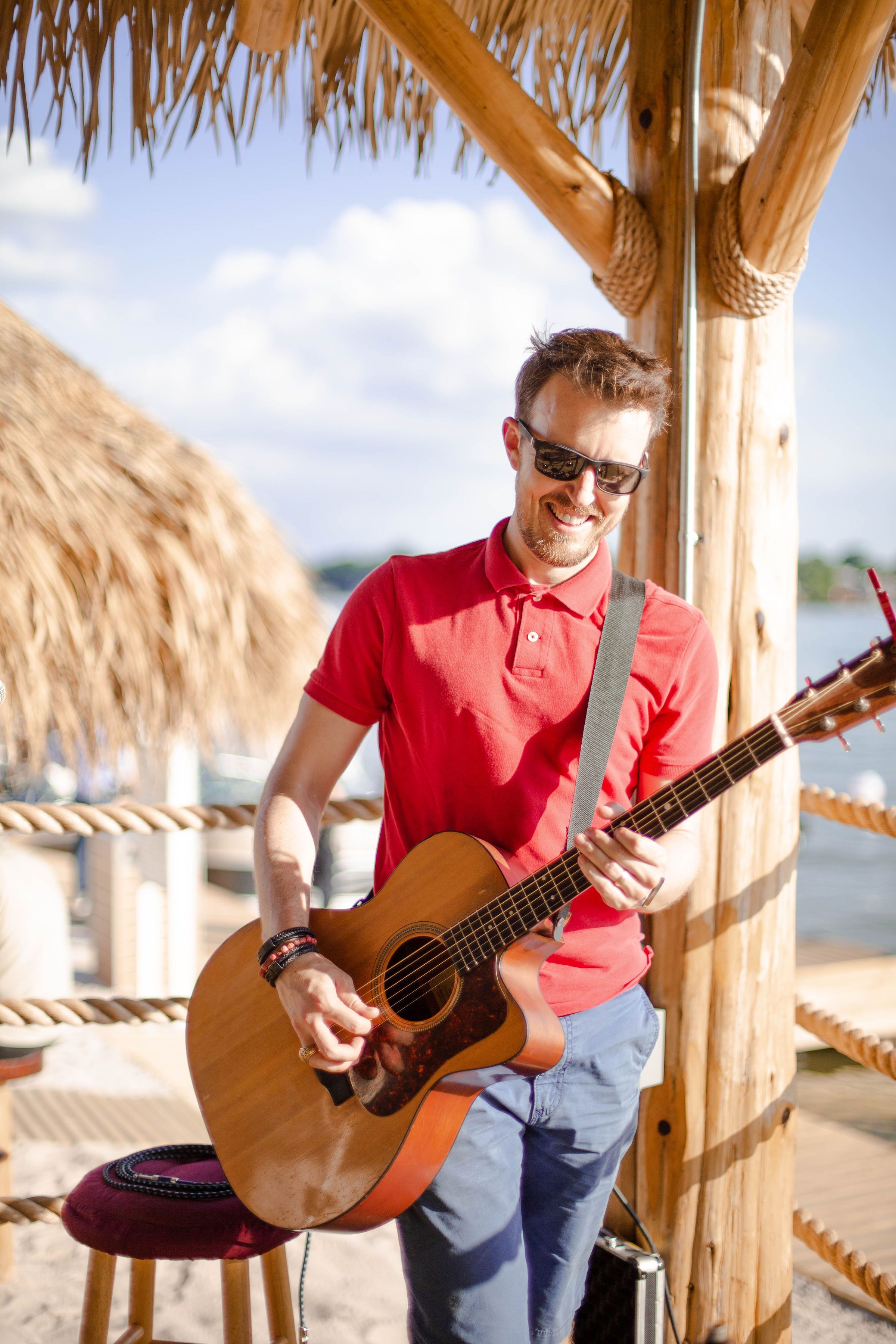 A person playing a guitar under a wooden structure with a rope railing.