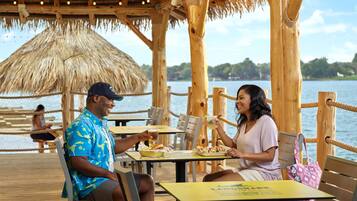 A wooden deck with tables and chairs, overlooking a body of water.