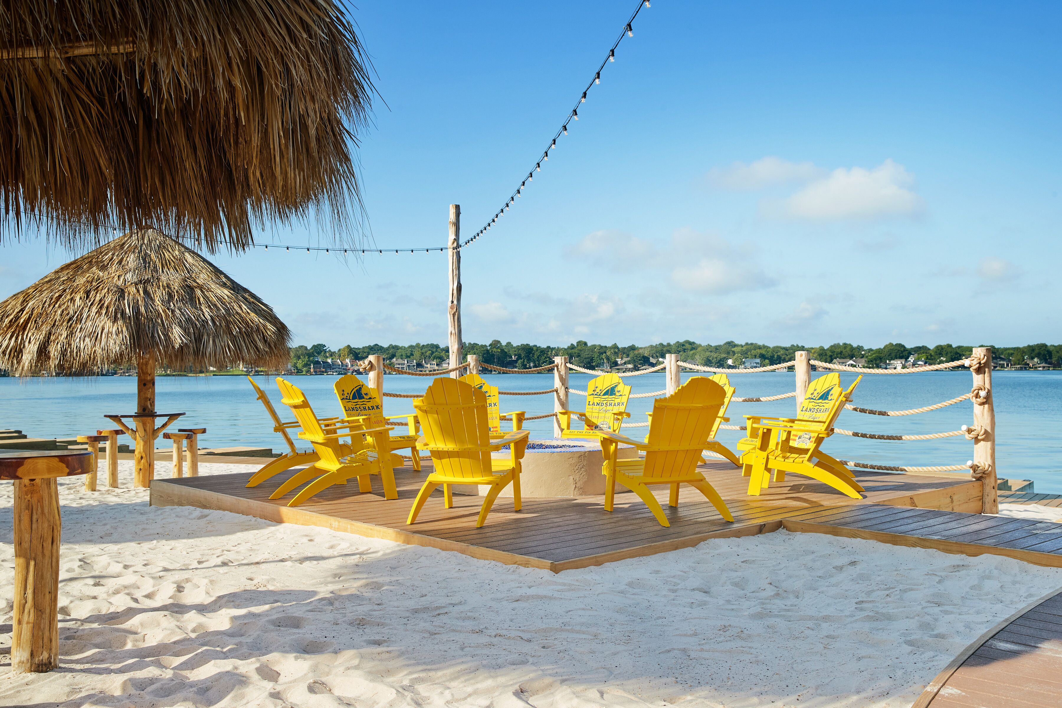 A beachside area with yellow Adirondack chairs, a thatched-roof structure, and a wooden deck overlooking a body of water.