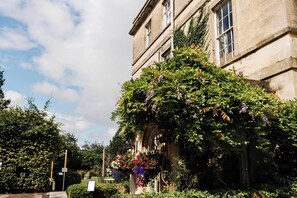 Un edificio histórico con jardín, fachada de piedra y una maceta colgante de flores.