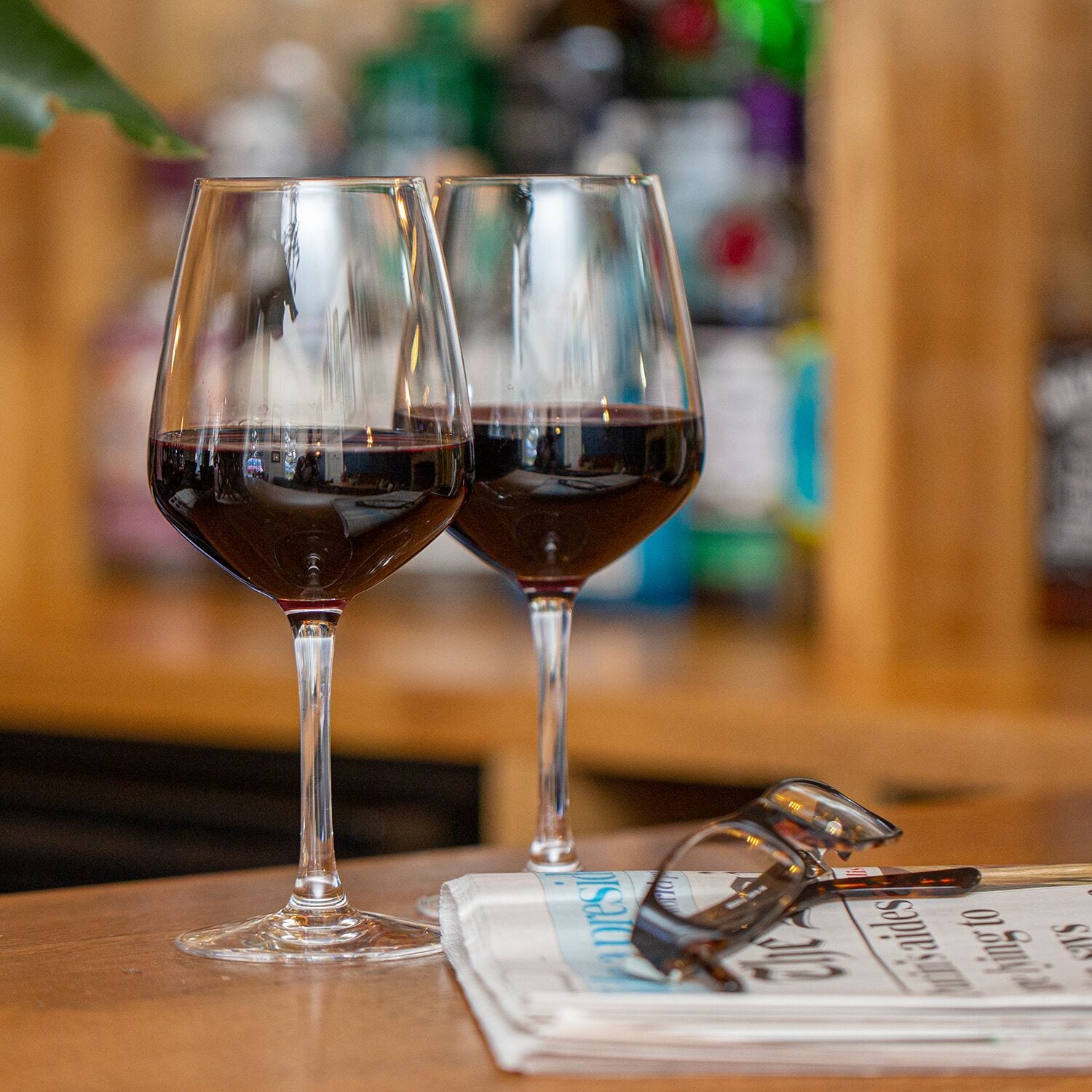 Two wine glasses on a wooden table with a pair of glasses and a menu.
