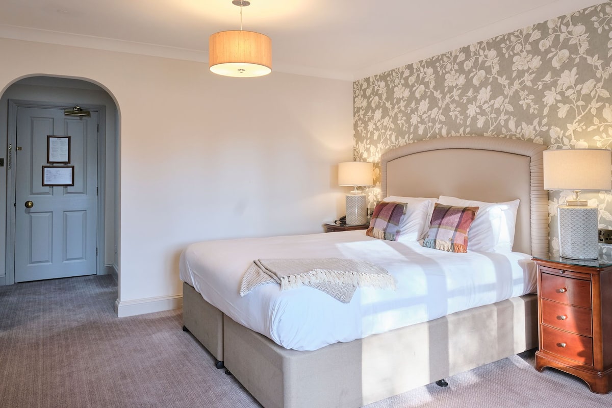 Quarto bem arrumado com uma cama grande, duas mesas de cabeceira com luminárias, cômoda de madeira e papel de parede floral.
